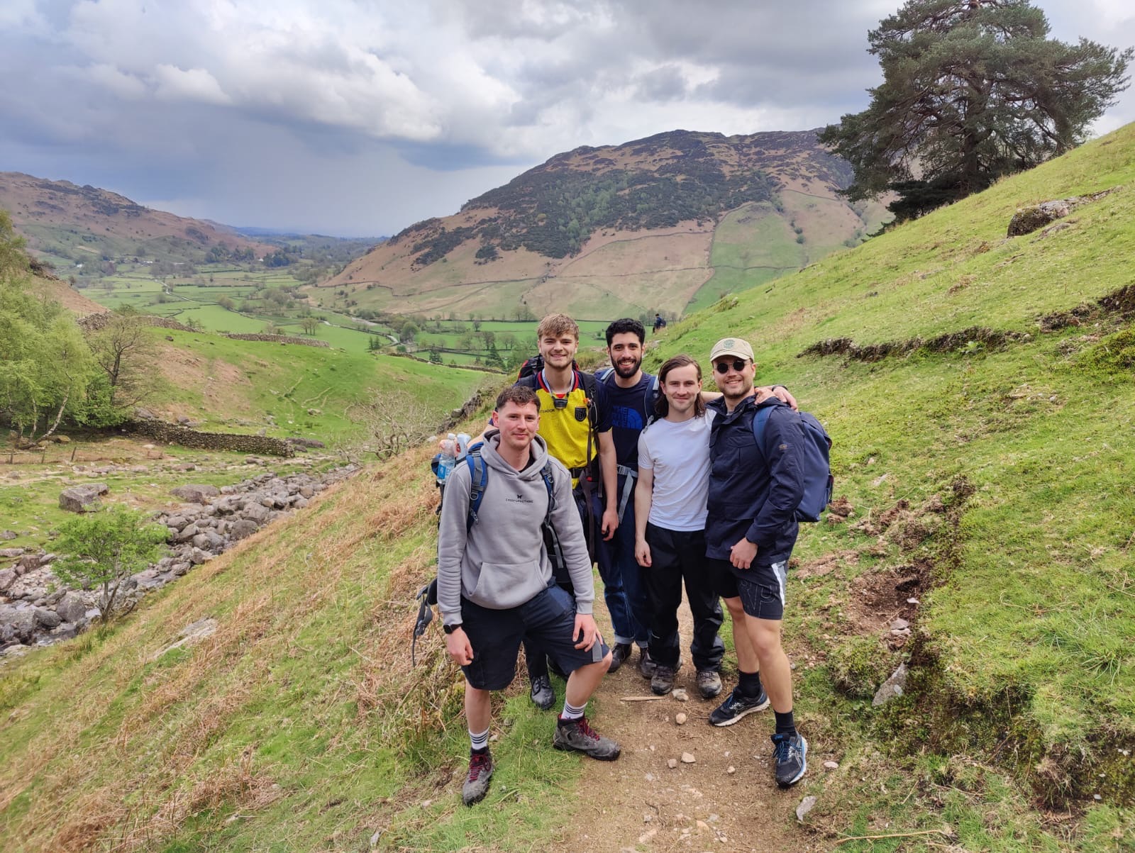 Five men with backpacks on a mountain trail in green hills